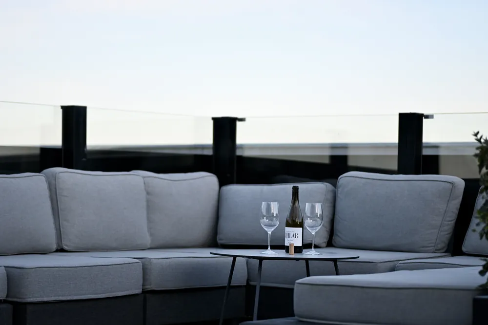 Terrassloungen på våning 19 i skymningen, vin på bordet och staden nedanför