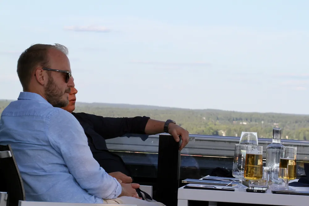 Gäst med en öl på terrassen på våning 19, skogen och Växjö i kvällssol