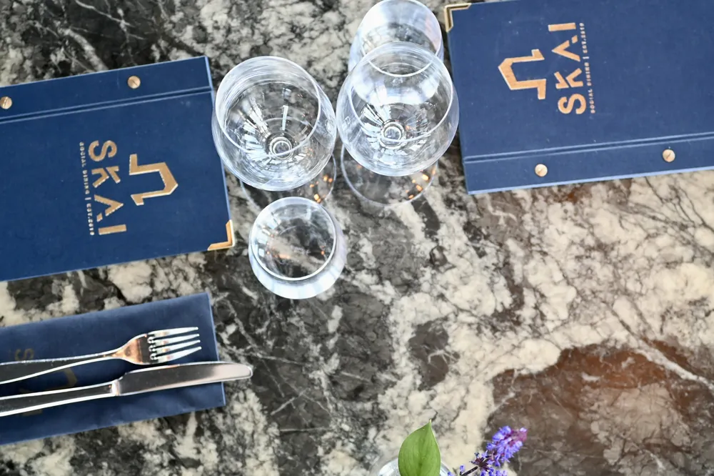Dukat bord på SKAI med menyn i blått omslag, glas och bestick på stenbordet