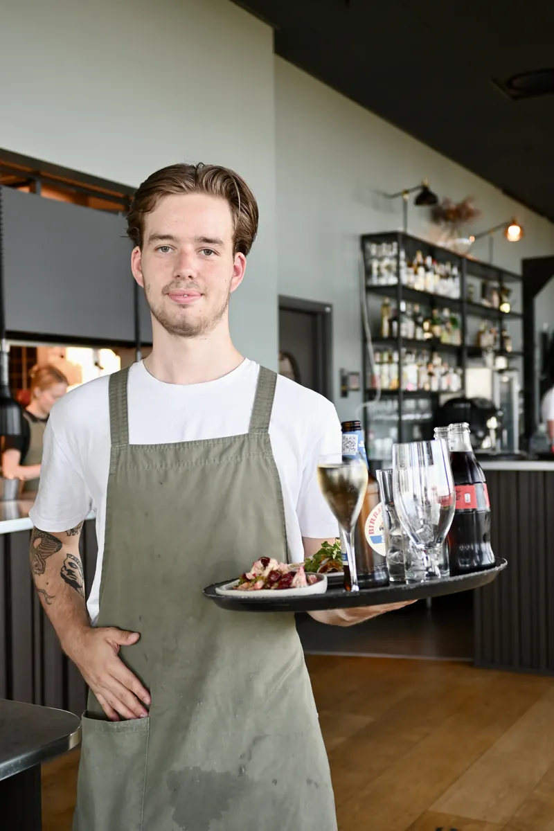 Servitör på SKAI med en bricka i handen, baren i bakgrunden