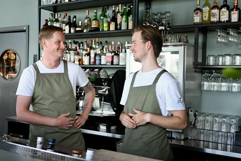 Två bartendrar bakom disken på SKAI, flaskhyllan bakom dem