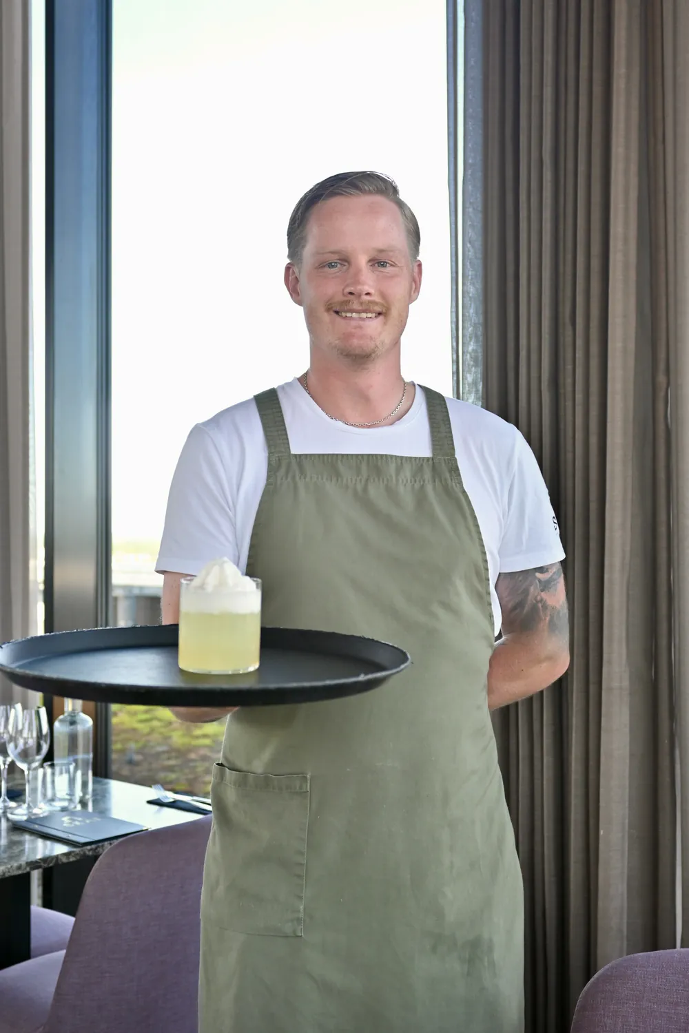 Servitör på SKAI med en bricka med dryck, matsalens fönster i bakgrunden